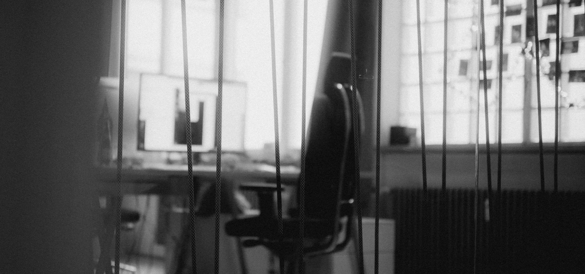schwarz weiß Abbildung eines Bürostuhls in einem Büro. Im Vordergrund sind Streben zu sehen, alles andere ist leicht verschwommen.